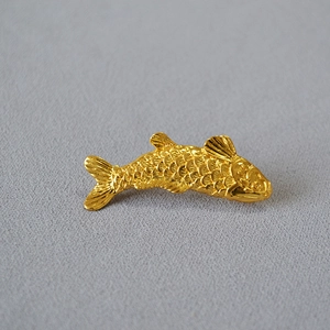 Macro shot of gold-plated koi fish brooch with detailed scales on grey fabric