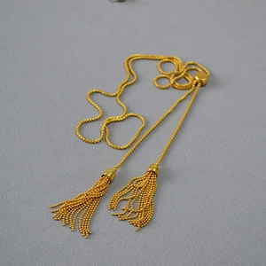 Macro shot of gold bead chain necklace featuring elegant double tassels and adjustable bolo slider