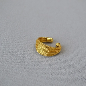 Détail macro d'une bague multicouche en laiton doré avec texture tressée et embouts polis