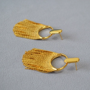 Détail de boucles d'oreilles luxueuses en maille dorée sur tissu texturé gris
