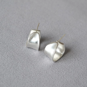 Macro detail of irregular C-shape matte silver earrings with textured ribbon design
