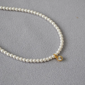 Detail shot of elegant small pearls necklace with a gold crystal pendant on grey fabric