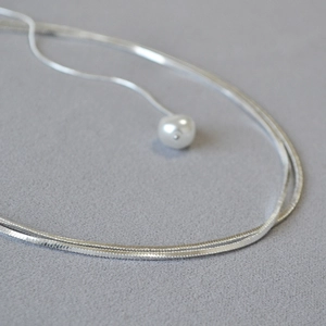 Vue macro d'un collier en maille serpent argentée avec un pendentif perle blanche minimaliste