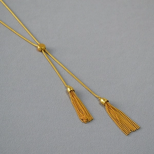 Detail of adjustable golden tassel necklace featuring a sliding round buckle and fine chains