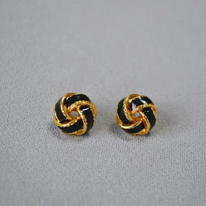 Détail macro de boucles d'oreilles émaillées noires dorées sur tissu texturé gris