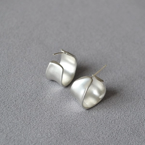 Macro shot of silver C-shaped earrings with wavy texture and matte finish detail