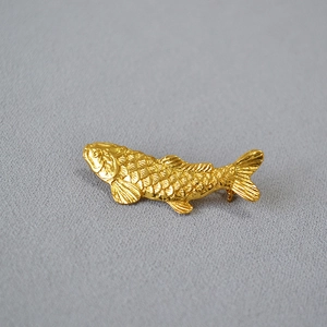 Vintage golden koi fish brooch with detailed scales on a grey textured background