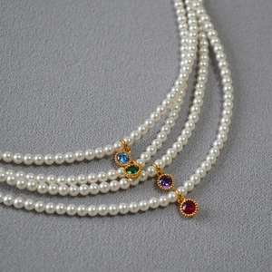 Macro detail of three-layer pearl necklace with colorful gemstone pendants in gold bezel