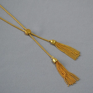 Macro detail of adjustable slider bead and double tassels on golden vintage sweater necklace
