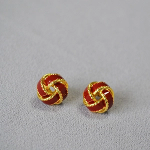 Détail macro de boucles d'oreilles émaillées rouges avec texture en métal tressé doré