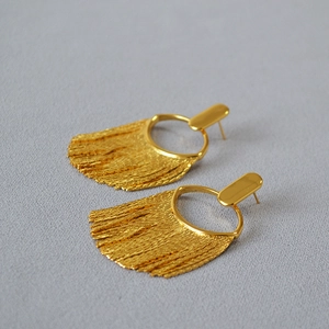 Gros plan de boucles d'oreilles pompons dorées avec détails de franges texturées