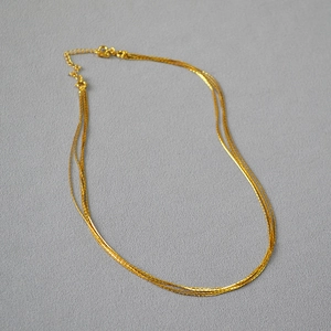 Detail of minimalist layered gold necklaces featuring fine chains and lobster clasp closure