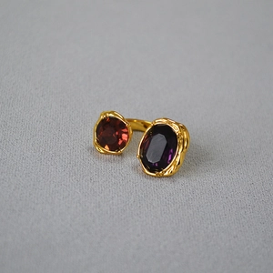 Dettaglio anello dorato regolabile con pietre rosse e viola e finitura strutturata