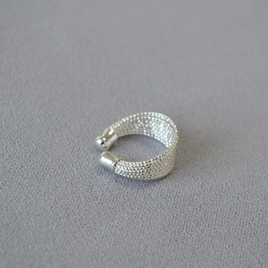 Détail de la bague en maille argentée avec extrémités sphériques polies sur tissu gris