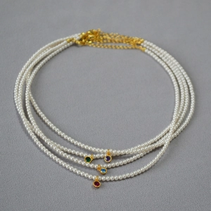 Detail of colorful gemstone pendants on white round pearl necklaces with gold lobster clasps