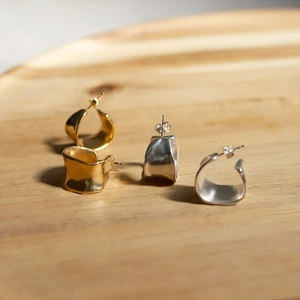 Irregular textured C-shaped wave earrings in gold and silver finish on wooden surface