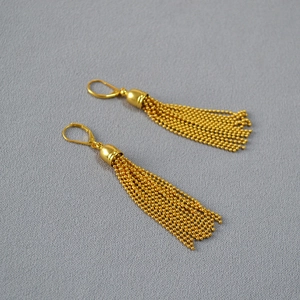 Detailed close-up of golden tassel drop earrings with delicate ball chain clusters