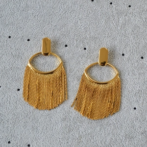 Détails de boucles d'oreilles dorées avec clous ovales et longues franges en chaîne