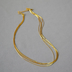 Detail of minimalist layered gold necklace featuring four thin chains and lobster clasp