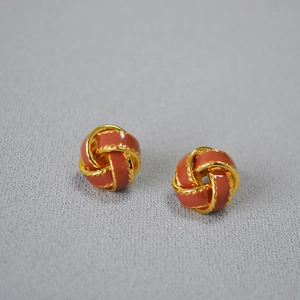 Détail de boucles d'oreilles rétro en laiton doré tressé avec émail orange et texture