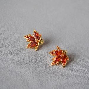Funkelnde orangefarbene Ahornblatt-Ohrstecker in Gold-Finish auf grauem Hintergrund