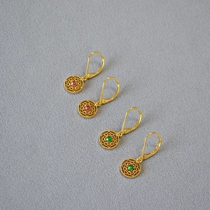 Détail macro de boucles d'oreilles en dentelle dorée avec pierres roses et vertes serties