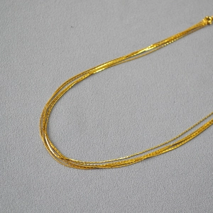 Detail of minimalist multi-layered gold skinny necklaces on dark textured fabric