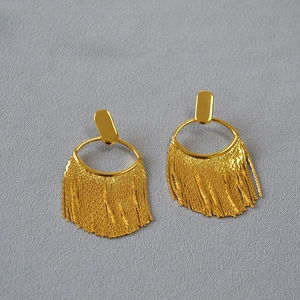 Vue détaillée des boucles d'oreilles pendantes à pompons longs plaqués or sur tissu gris