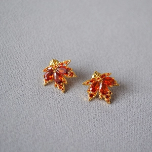 Funkelnde Ahornblatt-Ohrringe mit orangen Zirkonia und vergoldetem Finish auf grauem Grund