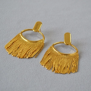 Détail de boucles d'oreilles à pompons dorés avec chaînes et clou en métal ovale poli