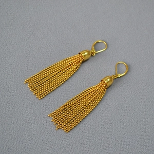 Close-up of golden beaded chain tassel earrings with vintage dome caps on grey fabric