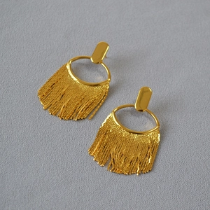 Détail de boucles d'oreilles pampilles dorées avec fines chaînes serpentines sur gris