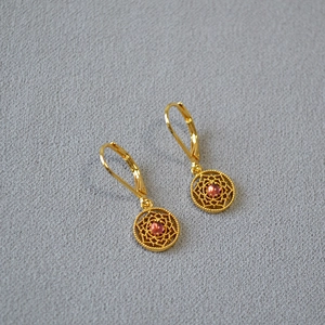 Détail de boucles d'oreilles dorées avec motif dentelle et pierres roses