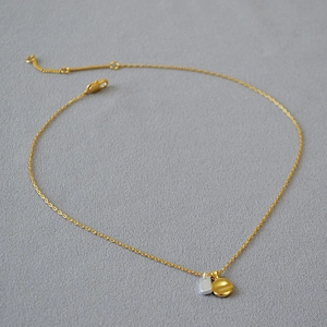 Detail of brass necklace with gold round pendant and silver rectangle charm on grey fabric
