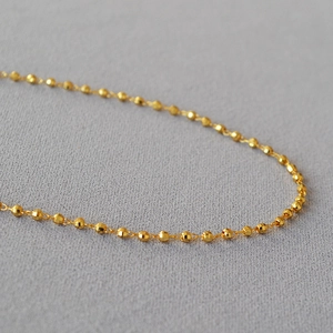 Vue macro d'un collier en laiton plaqué or avec billes facettées et reflets brillants