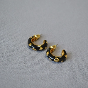 Detail view of retro C-shaped earrings with black enamel and embossed gold hearts