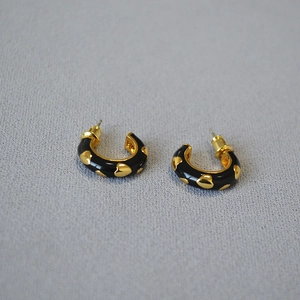 Detailed macro view of black enamel C-shaped earrings with gold heart embossing