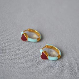 Macro view of mint green enamel hoop earrings with a detailed dark red heart pattern