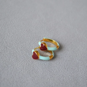 Close-up of gold hoop earrings with light blue enamel and a red heart charm detail