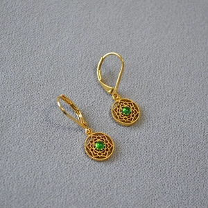 Gros plan de boucles d'oreilles filigranes dorées avec détail de pierre verte centrale