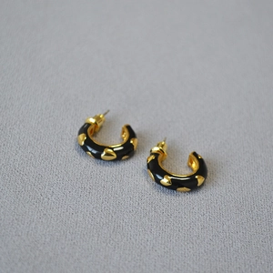 Detail of C-shaped gold-plated brass earrings with black enamel and small golden hearts