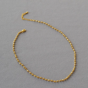 Détail d'un collier en perles dorées facettées avec fermoir homard et chaîne d'extension fine