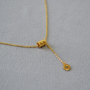 Vue macro du pendentif cylindre en laiton doré et de la chaîne à maillons fins
