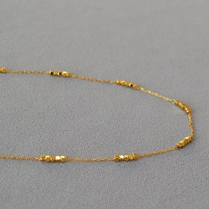 Minimalist 18k gold plated brass necklace with faceted square beads on grey fabric