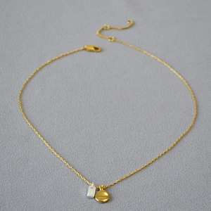 Macro detail of minimalist two-tone silver and gold pendants on a delicate necklace chain
