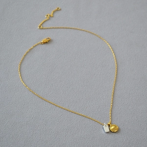 Detail of minimalist gold chain with dual-tone bean and silver rectangular pendants