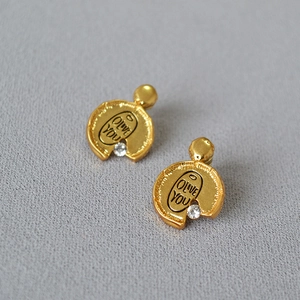 Detail of irregular matte gold earrings with zircon inlay and 'OLIVE YOU' engraving