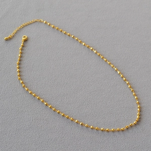 Détail du collier à perles facettées dorées montrant la finition or 18K et le fermoir mousqueton