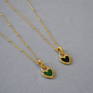 Détail de pendentifs en cœur avec incrustation verte et noire et chaîne dorée
