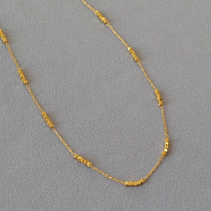 Macro view of gold-plated square beads on a fine chain necklace over grey fabric